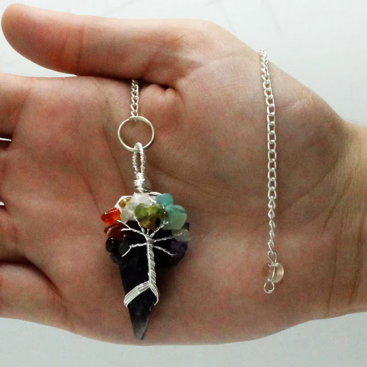 Hand holding a necklace with a multicolored stone pendant on a plain background